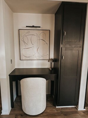 Une pièce comprenant un bureau en bois foncé, un pouf rond blanc, une armoire en bois foncé et une œuvre d’art abstraite accrochée au mur.