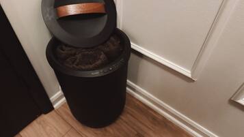 A trash can with a lid and a black trash bag inside.
