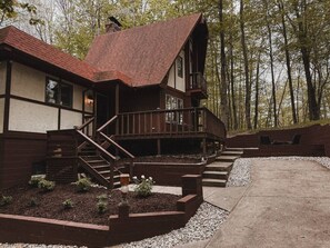 A two-story wooden cabin with a red roof, a balcony, and a staircase leading to the upper level.