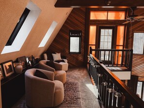 A loft-style room with a sloped ceiling, a wooden staircase, and a seating area with sofas and a rug.