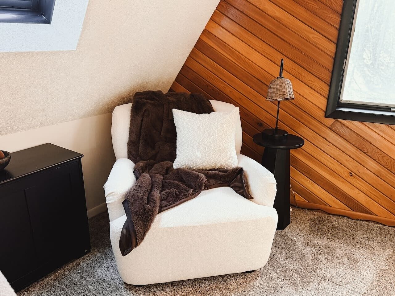 A massage chair with a blanket and pillows, a small table with a lamp, and a wooden wall.