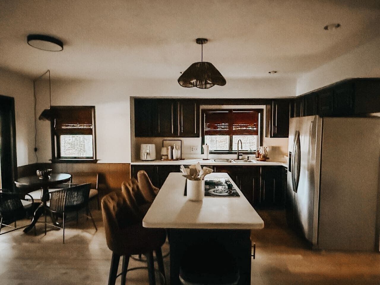 A modern kitchen with a central island, dark cabinetry, and a stainless steel refrigerator.