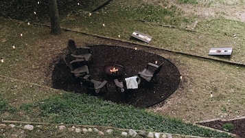 An outdoor seating area with a fire pit surrounded by chairs and a table, set on a grassy lawn with a stone border.