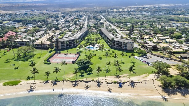 An aerial view of a resort with a central pool, palm trees, and a beach. - Beachfront 4BR, 2 Condos for 12 in Kihei, Maui! (Kihei)