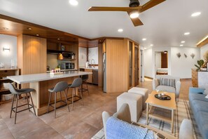 Una cocina moderna con una isla central, taburetes de bar y un comedor con sofá y mesa de centro.