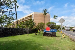 A hotel sign with a stone base and a blue signboard, located in front of a multi-story building with balconies. - Kihei, Maui Sunset, Spacious 4 BR, Beachfront, Sleeps 12 (Kihei)