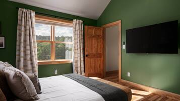 Una camera da letto con un letto, una finestra con tende, una porta in legno e una TV a schermo piatto montata a parete.