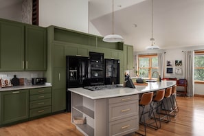 A modern kitchen with green cabinets, a black refrigerator, and a central island with bar stools. - Stylish & Modern Cabin: Hot Tub, Sauna, Pickleball (Berkeley Springs)