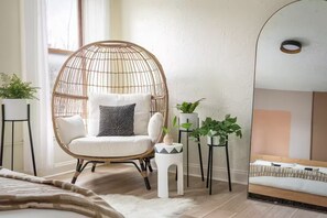 A room with a round wicker chair, a bed with a headboard, and two potted plants. - C-Street Art Loft (Springfield)