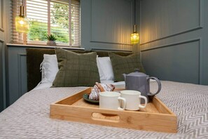Ein ordentlich bezogenes Bett mit einem Frühstücksbrett, einem Wasserkocher und einem Fenster mit Jalousien.