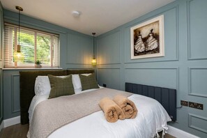 A bedroom with a bed, a window with blinds, a painting on the wall, and a bedside lamp. - No.6 Brantfell House (Bowness-on-Windermere)