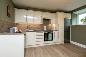 A modern kitchen with white cabinets, a built-in oven, and a stainless steel refrigerator. - No.6 Brantfell House (Bowness-on-Windermere)
