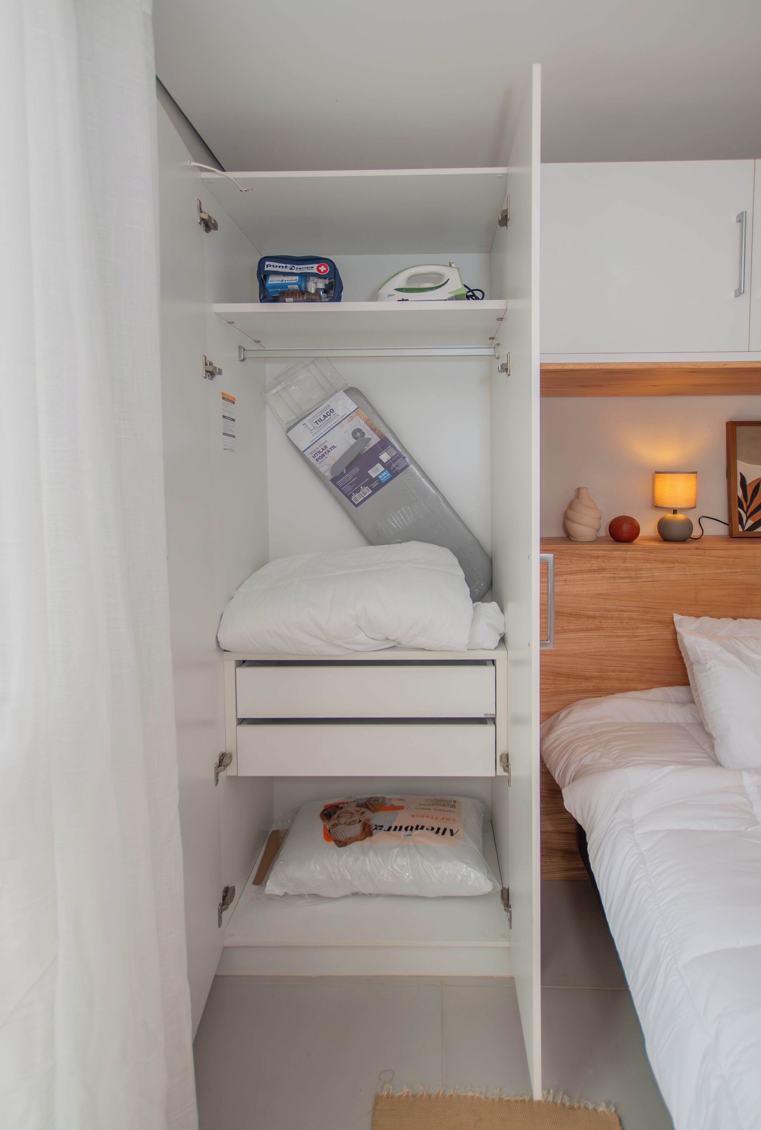 A bedroom with a bunk bed, a bedside table with a lamp, and a shelf with various items.