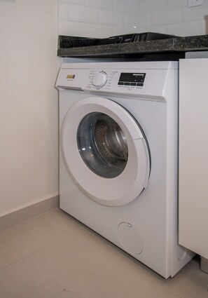 A front-loading washing machine with a control panel, located in a room with a tiled wall and a countertop above it. - Corporate Stays First Living - 906 (Asunción)
