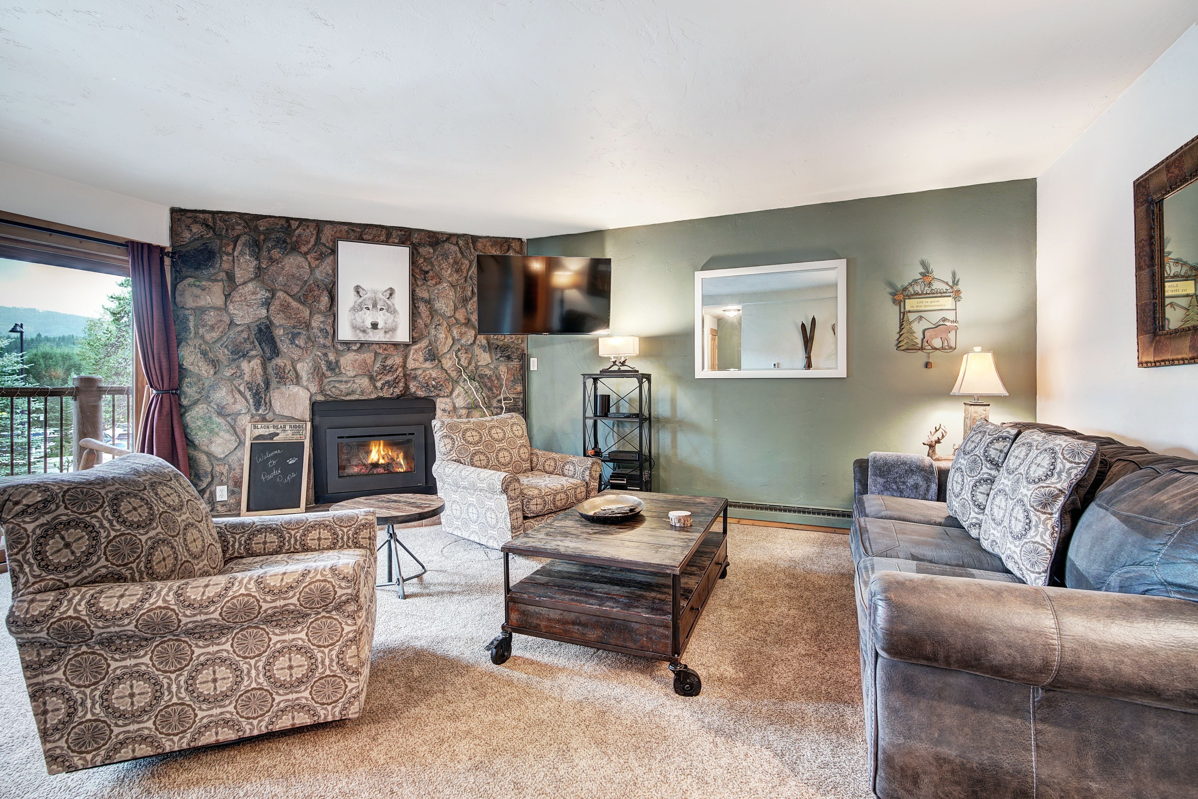 Una sala de estar acogedora con una pared de piedra, chimenea, muebles con diseño y vistas al exterior.