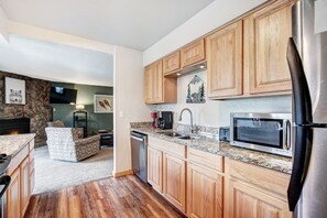 A modern kitchen with wooden cabinets, a stainless steel refrigerator, a microwave, and a dishwasher. - It's Four O'Clock Somewhere (Breckenridge)