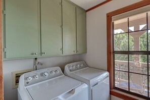 A laundry room with two stacked washers and dryers, a green cabinet above, and a window with a view of outdoor furniture. - River Access +EV + WI-FI+ Pets+ King+ Firepit (Hunt)
