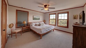 Ein Schlafzimmer mit einem Bett, einem Schreibtisch, einem Stuhl, einem Deckenventilator und zwei Fenstern.