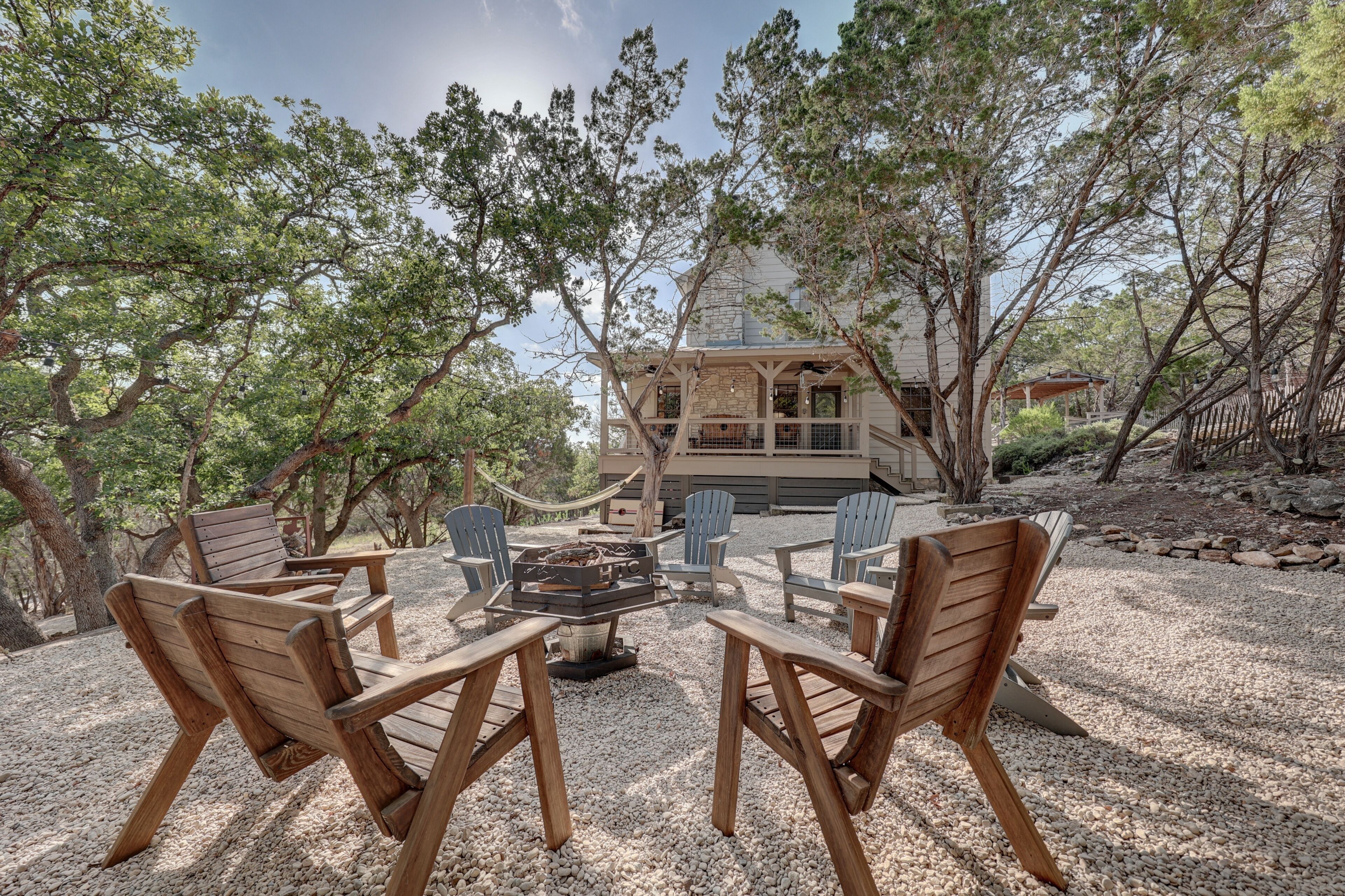 A wooden deck with Adirondack chairs and a fire pit, surrounded by trees.