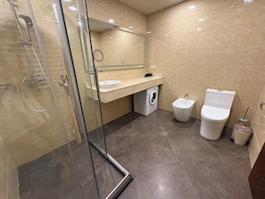 Ein modernes Badezimmer mit einer Duschkabine aus Glas, einer integrierten Waschmaschine, einem Bidet und einer Toilette.