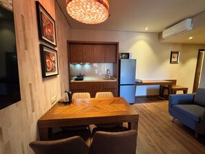Eine moderne Küche mit Holzausstattung, einer eingebauten Mikrowelle und einem Kühlschrank. Im Wohnbereich befindet sich ein Esstisch mit Stühlen sowie eine blaue Couch.
