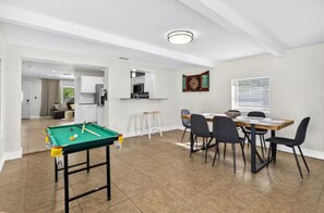 Een ruime kamer met een pooltafel, eethoek en keuken.