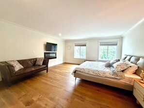 Un dormitorio con cama, sofá, televisor montado en la pared y dos ventanas.