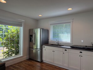 A kitchen with a stainless steel refrigerator, white cabinetry, a window with blinds, and a wooden floor. - Redwood 1-Acre Estate (Surrey)