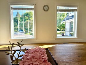 Una habitación con dos ventanas, un reloj en la pared y una planta decorativa sobre una mesa.