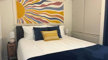 Een hotelkamer met een bed, nachtkastje, lamp, kledingkast en een schilderij aan de muur.