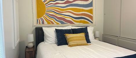 A bedroom with a bed, pillows, a nightstand, a lamp, and a wall art piece.