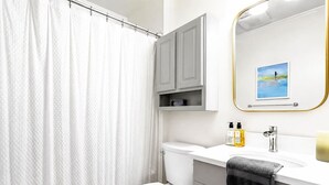 Un baño con cortina de ducha, inodoro, tocador con espejo y un cuadro en la pared.