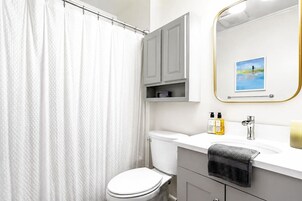 A bathroom with a shower curtain, toilet, vanity with a mirror, and a framed picture on the wall.