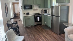 Una cocina con gabinetes verdes, un refrigerador de acero inoxidable, un microondas, una estufa y un lavamanos.