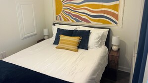 Una cama con ropa de cama blanca, cabecera azul y almohada decorativa.
