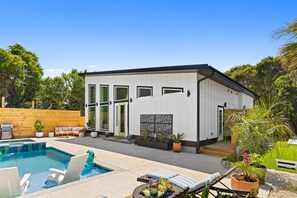 Una casa moderna con piscina, mobiliario exterior y cerca de madera.