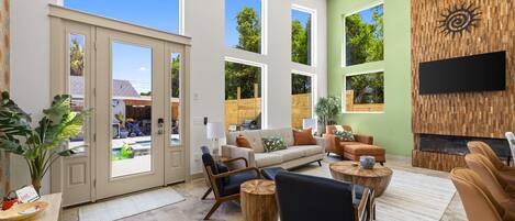 A spacious living room with large windows, a fireplace, and a flat-screen TV mounted on a wooden wall.