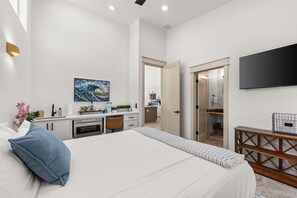 Ein modernes Schlafzimmer mit einem großen Bett, einem Schreibtisch, einem Fernseher und einem durch eine offene Tür einsehbaren Badezimmer.