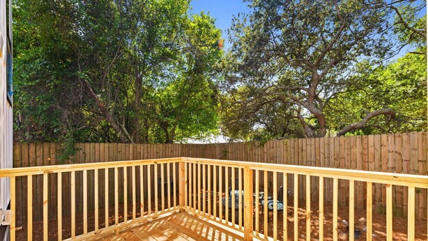 Une terrasse en bois dotée d’une rambarde, entourée d’une clôture en bois et d’arbres.