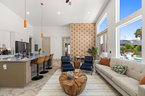 A modern kitchen with a bar area, a dining space with chairs, a sofa, and a large window. - 3 King Beds*Resort Pool*Private Beach Access (Panama City Beach)