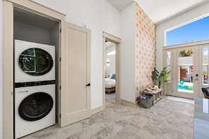 A laundry room with a front-loading washer and dryer, a hallway leading to a bedroom, and a view of a swimming pool through an open door. - 3 King Beds*Resort Pool*Private Beach Access (Panama City Beach)