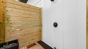 Une clôture en bois, un pot de fleurs noir avec des plantes, et un mur blanc avec un robinet noir.