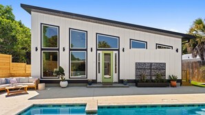 Une maison moderne à deux étages, dotée d’une piscine, de grandes fenêtres et d’une porte verte.
