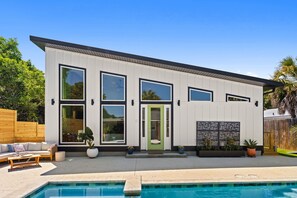 Ein modernes, zweistöckiges Haus mit Schwimmbad, großen Fenstern und einer grünen Tür.