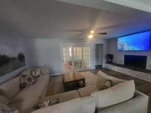 Ein Wohnzimmer mit einer Sofagarnitur, einem Kamin, einem Fernseher und einer Glasschiebetür, die zu einem Außenbereich führt.