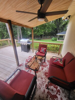 A covered outdoor seating area with a grill, a ceiling fan, and a view of a backyard.