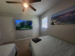 Een slaapkamer met twee bedden, een plafondventilator, een televisie aan de muur en een schilderij.