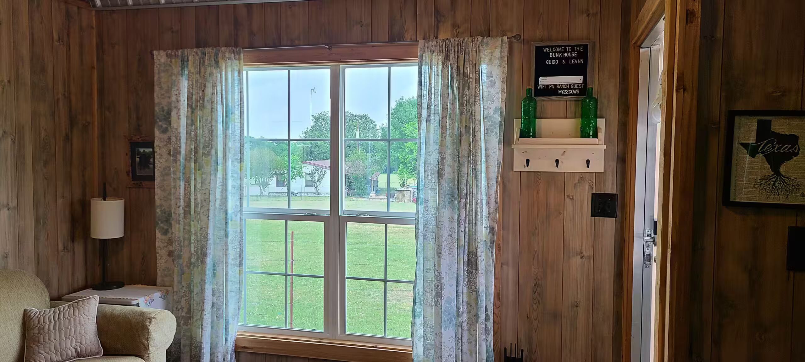 A room with wooden walls, a large window with curtains, a sign indicating WiFi availability, and a framed picture of a tree.