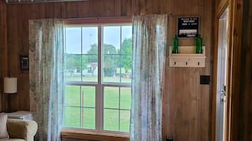 A room with wooden walls, a large window with curtains, a sign indicating WiFi availability, and a framed picture of a tree.