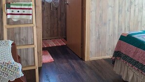 A cozy room with a wooden floor, a bed with a quilt, a wooden ladder, and a door leading to another room.